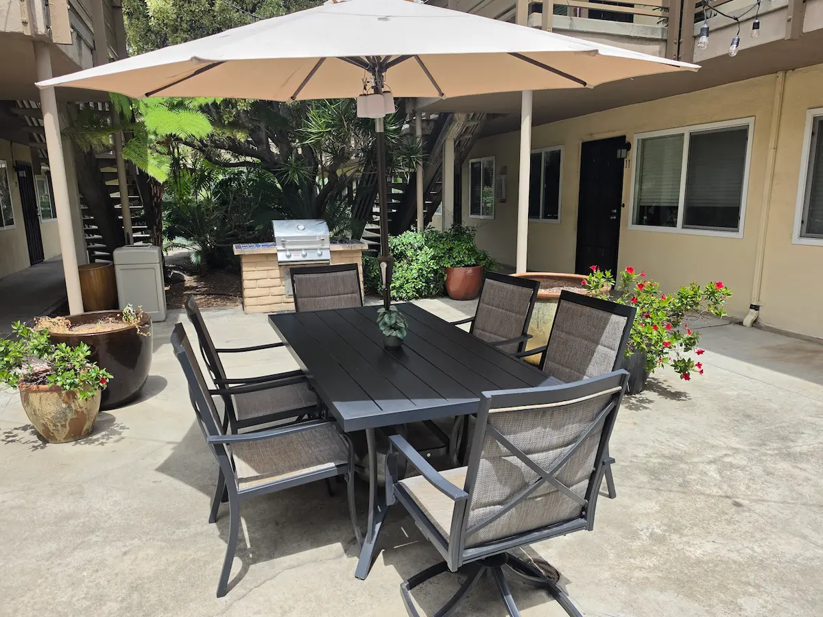 Courtyard dining area with umbrella, seating for eight, and gas grill